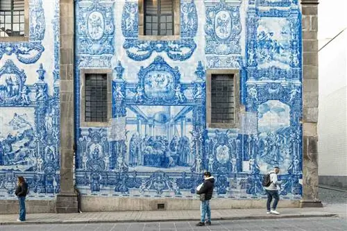 Люди идут мимо здания с синей плиткой в Порту