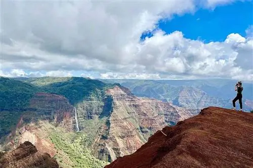 Человек на вершине горы фотографирует каньон Ваймеа.