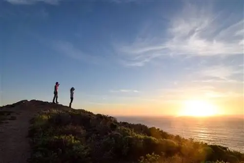 Два человека на холме наблюдают закат в Биг-Суре