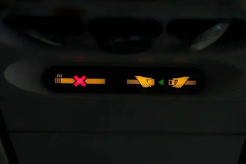 Знак «Пристегните ремень безопасности» и знак «Не курить» рядом с вентиляционным отверстием над сиденьями самолета