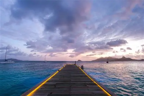 Длинный пирс в океан с лодками и горами на закате из курорта и спа-салона Palm Island в Гренадинах