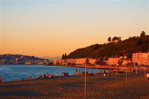 Пляж Алки во время золотого часа в Сиэтле с людьми, выстроившимися вдоль пляжа и наблюдающими за закатом.