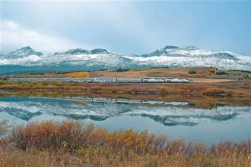 Вид на Empire Builder компании Amtrak, идущий вдоль заснеженных гор и осенней листвы.