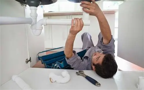 Сантехник работает на трубах под кухонной раковиной