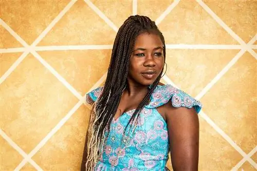 Хаджоу Самбе перед стеной с желтым узором в своем доме в Сенегале.