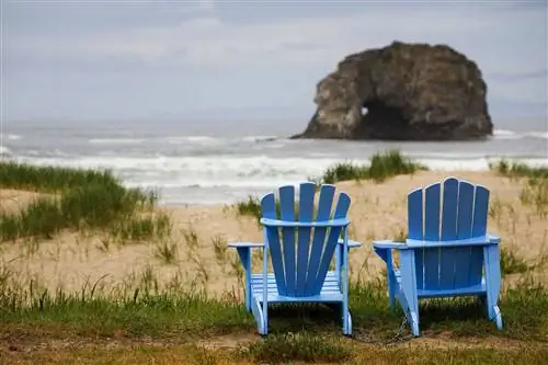 Два синих кресла Adirondack на травянистом пляже Rockaway в Орегоне