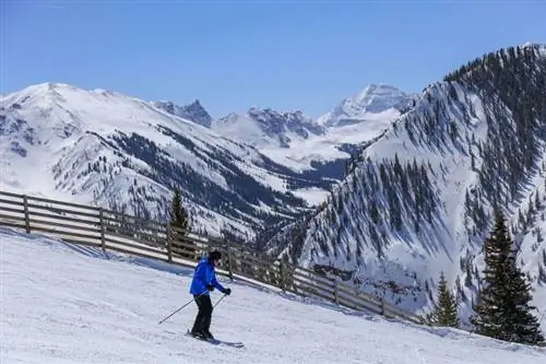 Мужчина в синей куртке катается на горных лыжах на фоне Maroon Bells of the Rocky Mountains на горнолыжном курорте Аспен Сноумасс.