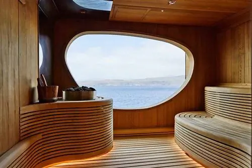 Изогнутая деревянная конструкция в сауне на круизном лайнере с окном, выходящим на воду и зеленые холмы