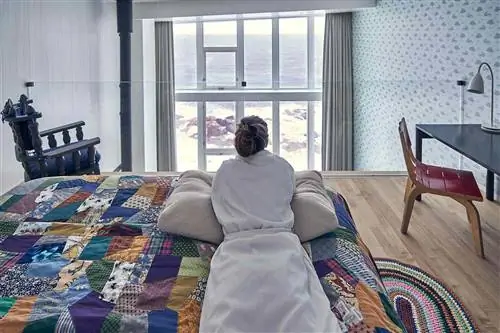 Женщина в банном халате лежит на кровати в номере Fogo Island Inn.