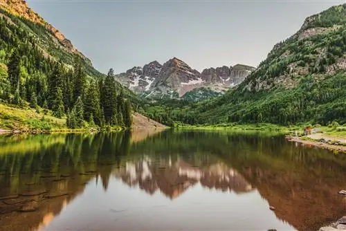 Maroon Bells сидят тихо, когда солнце в середине лета садится на достопримечательность Аспена, штат Колорадо.