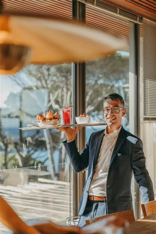 мужчина балансирует поднос с напитками и едой. солнечный свет. улыбка