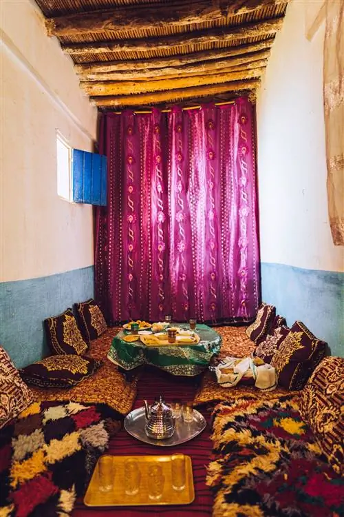 узкая комната. пурпурный занавес. еда на полу. подушки. Серебряный чайник. красочная и декоративная ткань