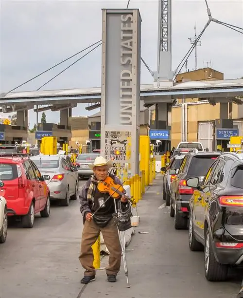 Пожилой человек играет на скрипке среди десятков машин, стоящих в очереди на мексиканской стороне, ожидающих пересечения границы с Соединенными Штатами до пандемии.