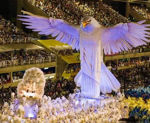 Женщины, участвующие в параде самбы, танцуют самбу на вершине богато украшенной платформы. Все участники одеты в изысканные костюмы.