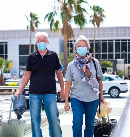 Старшая пара с багажом и маской в аэропорту