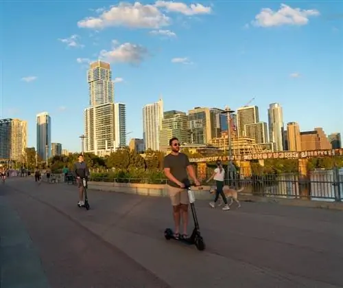 Езда на скутерах через реку Колорадо или городское озеро по пешеходному мосту в центре Остина, штат Техас, на закате