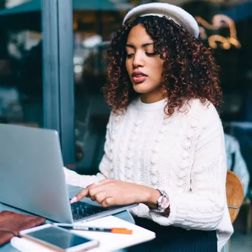 Серьезная темнокожая кудрявая женщина, печатающая на ноутбуке, делится контентом в блоге, просматривая веб-страницы и информацию, задумчивая африканская американка-фрилансер, выполняющая удаленную работу на террасе кафе