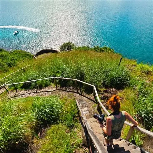 Женщина спускается по лестнице в национальном парке Пиджен-Айленд, историческом и натуралистическом месте, которое включает в себя руины форта Родни и множество тропинок, вьющихся среди деревьев и открывающих захватывающий вид на побережье.