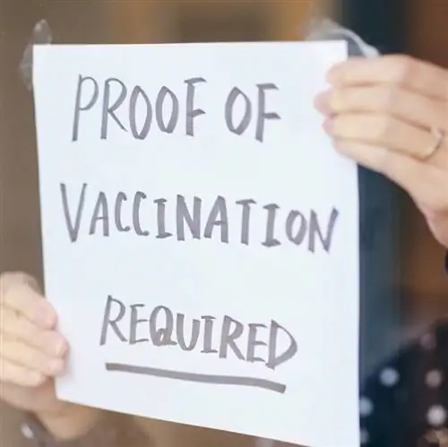 Владелец магазина держит знак, подтверждающий необходимость вакцинации