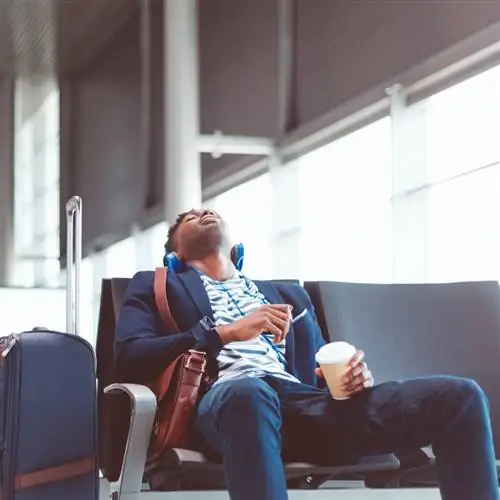 измученный путешественник в аэропорту спит на своем месте. чемодан рядом и кофе в руке