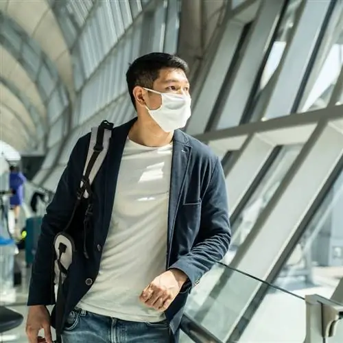 путешественник в маске ждет посадки в самолет, стоит в терминале вылета в аэропорту.