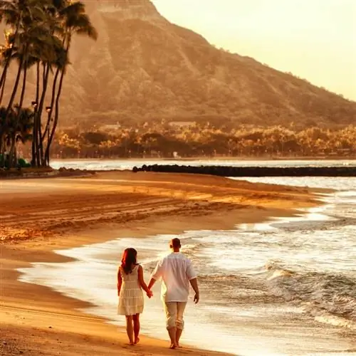 Фотография счастливой молодой пары, идущей рука об руку по пляжу Вайкики на рассвете.