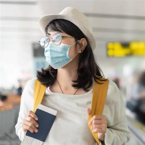 Азиатская женщина сжимает свой паспорт в маске в неизвестном аэропорту