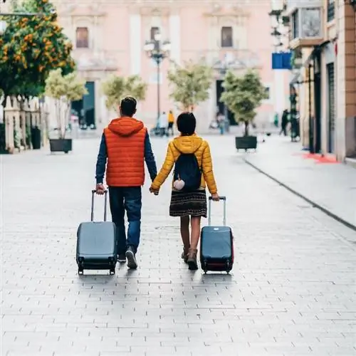 Пара, держащая чемоданы на колесиках рука об руку, гуляет по улицам Европы
