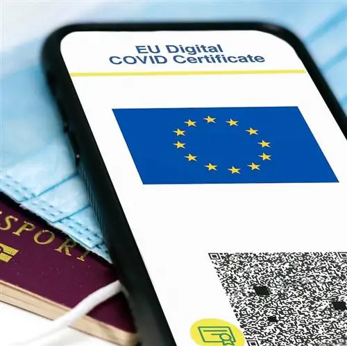 Цифровой сертификат ЕС COVID с QR-кодом на экране мобильного телефона поверх хирургической маски и паспорта
