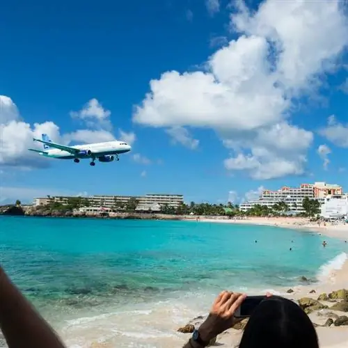Люди на пляже Махо наблюдают, как самолет JetBlue Airbus A320 заходит на посадку в международном аэропорту Принцессы Юлианы на острове Синт-Мартен. Люди используют смартфоны и iPod для фотографирования.