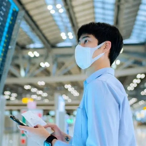 Молодой азиат в маске во время проверки табло вылета в аэропорту