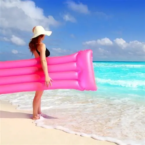 Туристка держит розовую надувную шезлонг, направляясь в океан в Канкуне, Мексика
