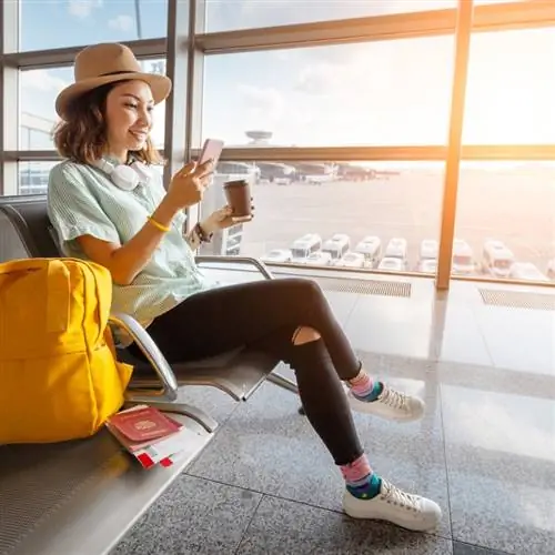 Счастливая азиатская путешественница в аэропорту проверяет свой телефон