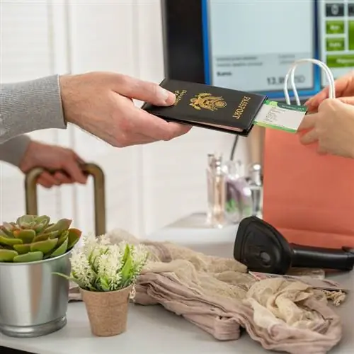 Мужчина протягивает американский паспорт с посадочным талоном кассиру в женском бутике в аэропорту беспошлинной торговли