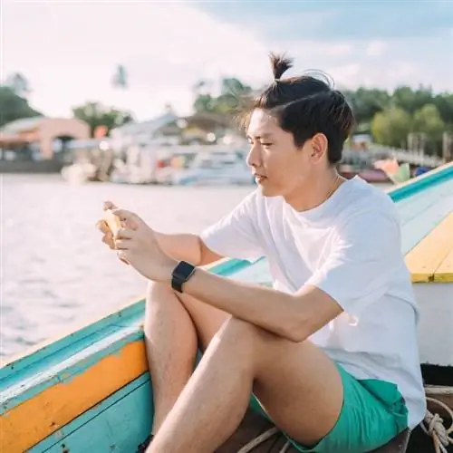 Молодой азиат пользуется мобильным телефоном во время прогулки на лодке с размытым видом на остров Пхи-Пхи, Таиланд