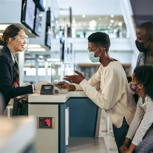 Пассажиры стоят у стойки регистрации с персоналом аэропорта на стойке регистрации в аэропорту.