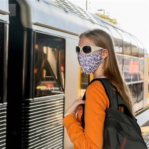 Женщина в цветочной маске из ткани садится в поезд