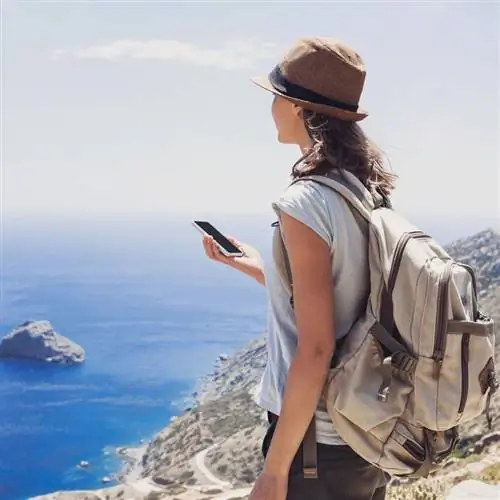 Путешественник поднимается в гору с мобильным телефоном в руке.