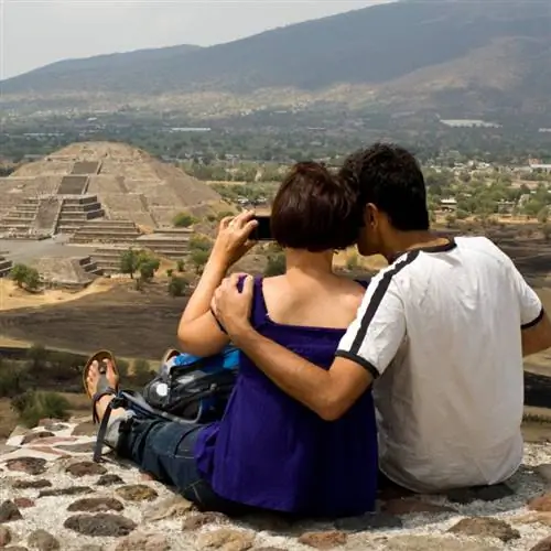 Пара туристов смотрит на пирамиду Луны в Теотиуакане, Мексика