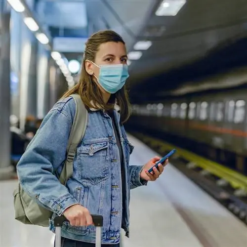 Молодая женщина в защитной маске с мобильным телефоном на станции метро