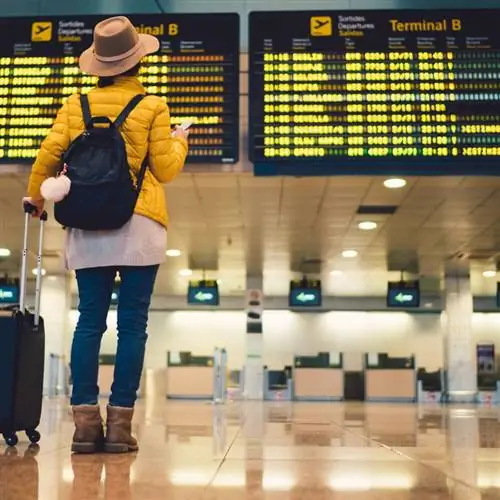 Женщина в терминале аэропорта проверяет табло вылета