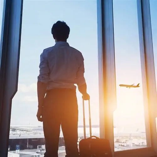 Мужчина стоит у терминала аэропорта и смотрит на взлетную полосу