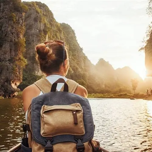 Женщина с рюкзаком плывет на лодке среди карстовых гор, чтобы встретиться со своими друзьями. Там Кок, север Вьетнама.