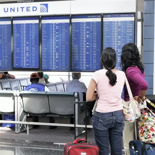 Две женщины-путешественницы смотрят на табло вылета рейса United Airlines в аэропорту