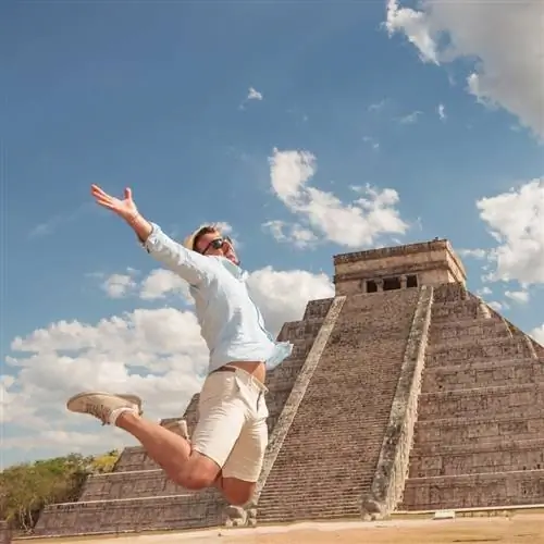 Молодой турист-мужчина прыгает от радости на фоне пирамид майя, Мексика