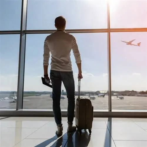 Уверенный молодой человек наблюдает, как самолет взлетает из зала вылета аэропорта