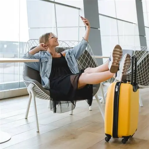 Молодая путешественница делает селфи, положив ноги на чемодан в зале ожидания аэропорта