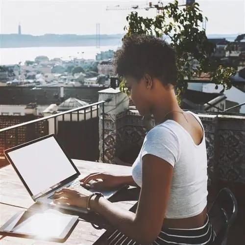 женщина работает на своем ноутбуке, сидя во внутреннем дворике с видом на город у океана в Португалии