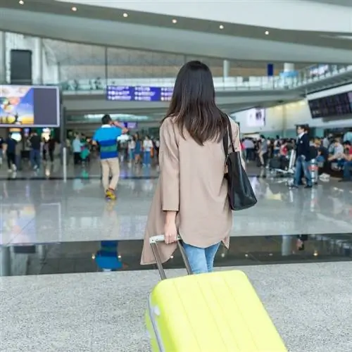 Женщина-путешественница тянет багаж, направляясь к стойкам регистрации в аэропорту, концепция воздушного путешествия