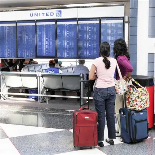 Две женщины-путешественницы смотрят на стойку регистрации Delta Airlines и доску объявлений в аэропорту